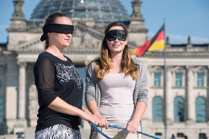 Zwei Frauen mit Augenbinde vor dem Reichstag in Berlin halten ein blaues Seil in den Händen.