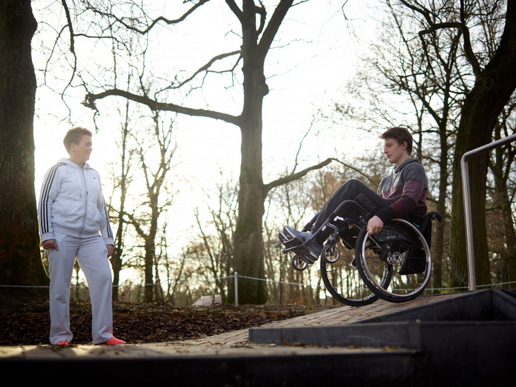 Eine Reha-Therapeutin mit einer Person im Rollstuhl draußen.