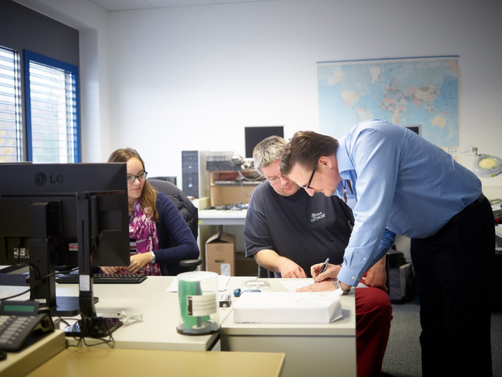 Teambesprechung zwischen drei Mitarbeitenden am Schreibtisch im Büro.