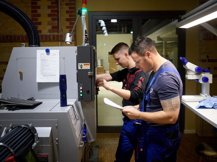 Zwei männliche Mitarbeiter in Werkstattbekleidung bedienen eine Maschine im Labor. 